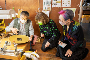 写真：MICHIKAKEの漆塗り作業を見学する荻野さん、残間さん